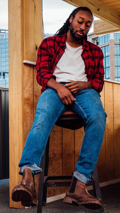 穿着红白格子衬衫和蓝色牛仔牛仔裤的男人坐在棕色的木头上